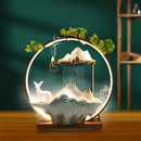 Decorative lamp with mountain, deer, and tree design on a wooden base.