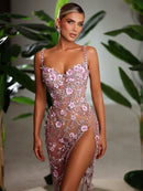 Woman wearing a pink floral dress with a blurred green plant background