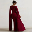 Woman wearing a burgundy evening gown with long sleeves and a slit on a plain background