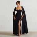 Woman wearing a black evening gown with a cape against a plain background