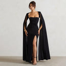 Woman wearing a black evening gown with a cape against a plain background