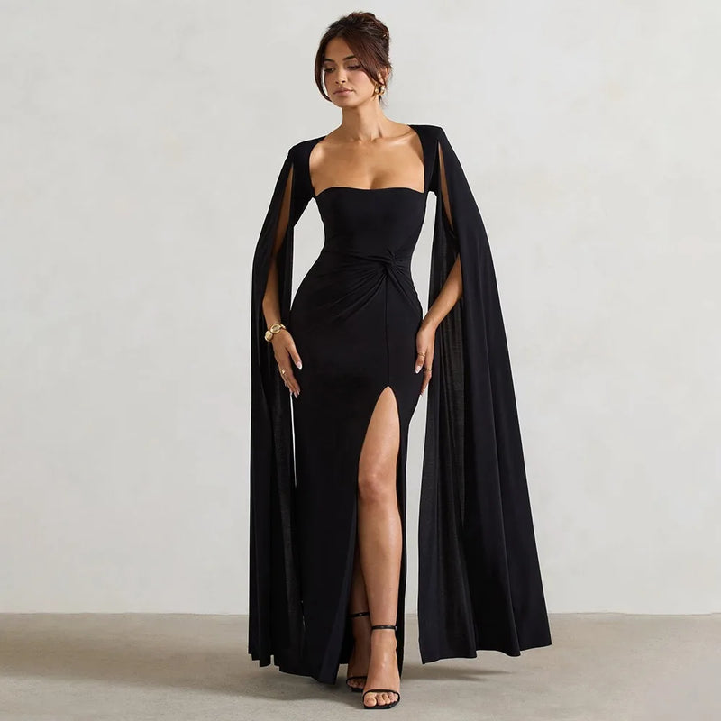 Woman wearing a black evening gown with a cape against a plain background