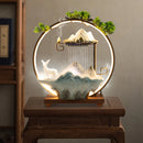 Decorative scene with mountains, deer, and waterfalls inside a circular frame on a wooden stand.