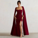 Woman wearing a burgundy evening gown with a cape against a plain background
