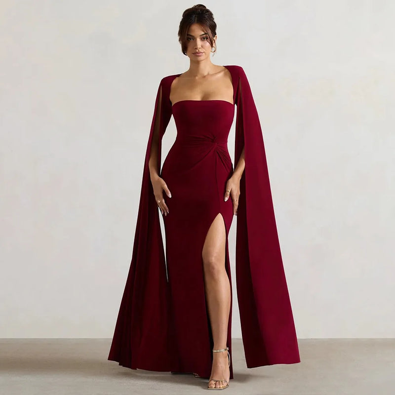 Woman wearing a burgundy evening gown with a cape against a plain background