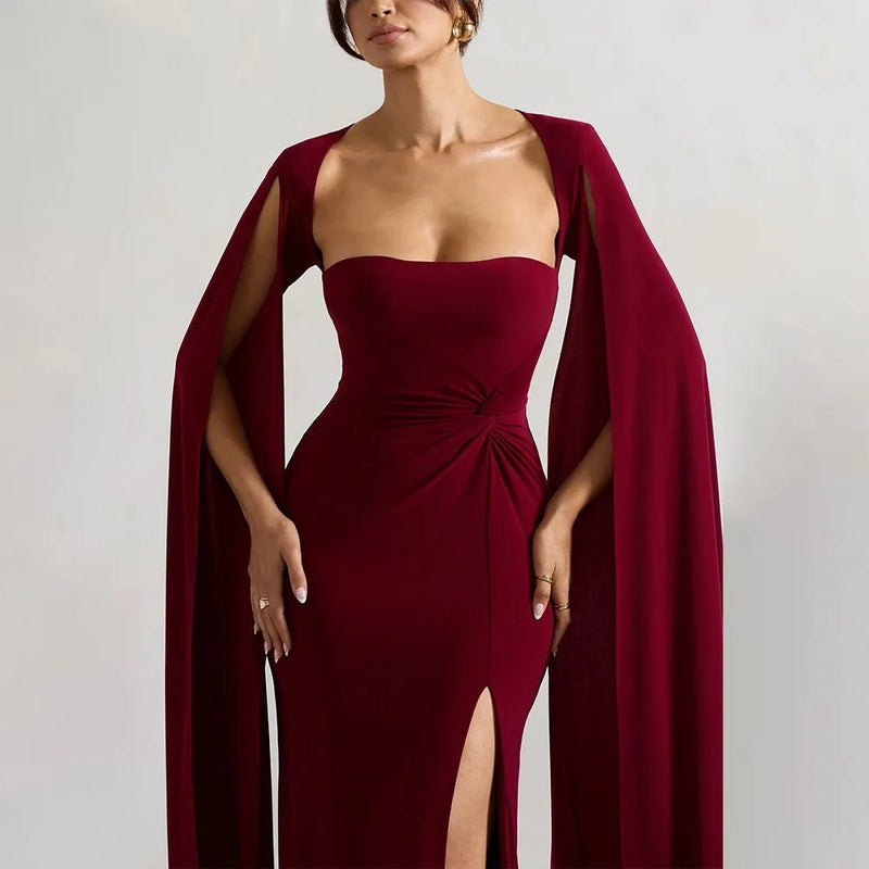 Woman wearing a burgundy evening gown with a cape on a plain background