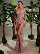 Model wearing a pink floral evening gown in a decorated indoor setting with plants.