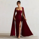 Woman wearing a burgundy evening gown with a cape against a plain background