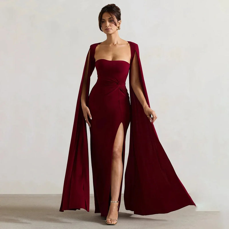 Woman wearing a burgundy evening gown with a cape against a plain background